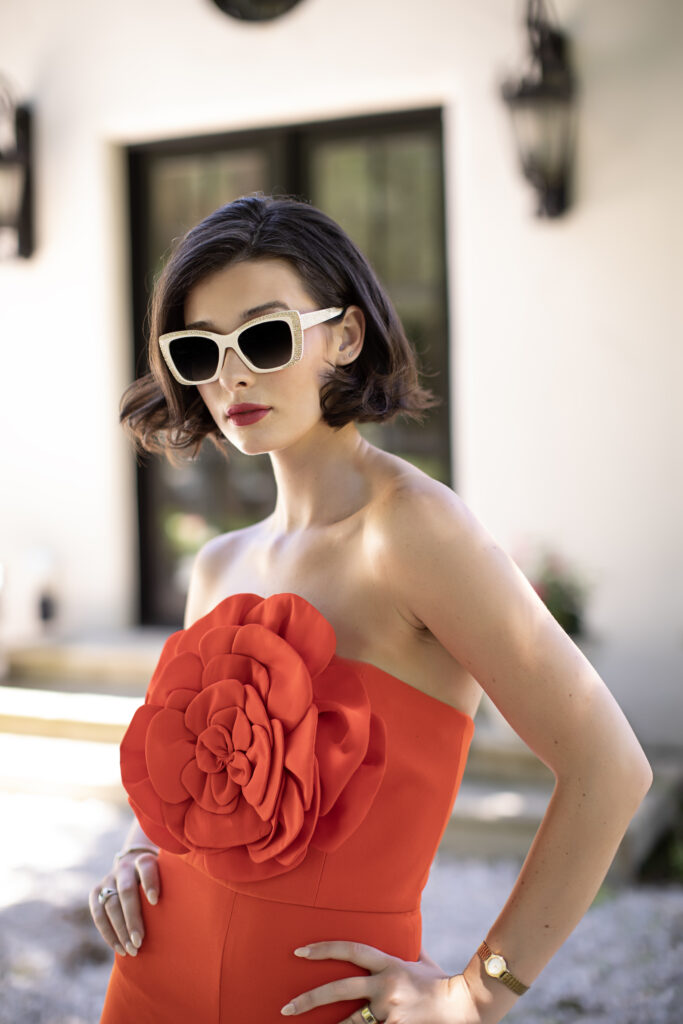 Model wearing Sospiri's sunglass Zora and posing in a orange jumpsuit. 